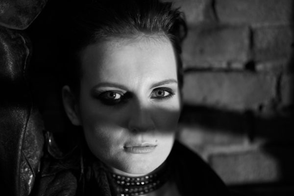 A woman leans against a brick wall at night in this black and white, high contrast portrait from the Sin City photo session