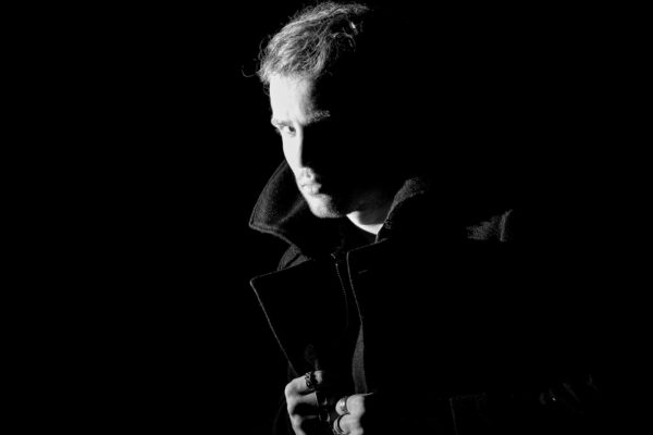 A model portrays a Sin City detective. He is wearing a black coat and hiding in the darkness of the night. This dramatic portrait is from the Sin City photo session