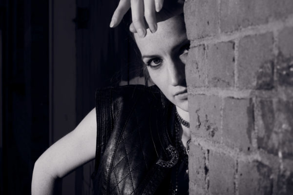 A model interprets a Sin City femme fatale hiding behind a brick wall at night in an Amsterdam neighborhood
