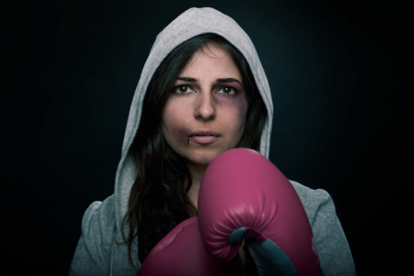 A dramatic portrait of a strong woman wearing boxing gloves and a grey hoodie taking a boxing stance